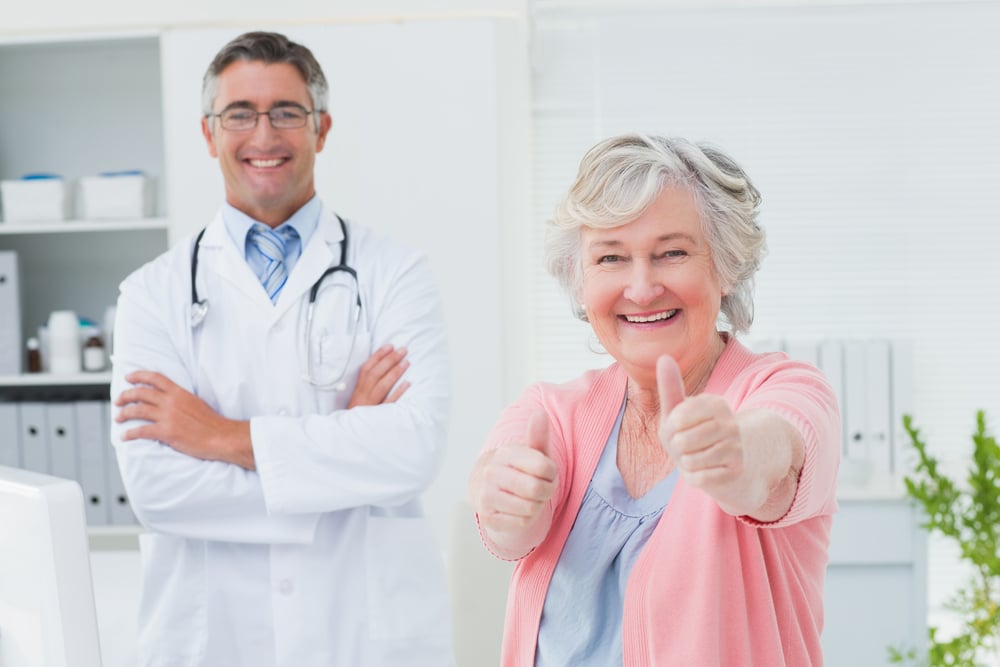 Portrait of happy female patient showing thumbs up sign while standing with doctor in clinic-1